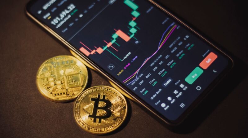 Smartphone showing a crypto trading app next to two bitcoin coins