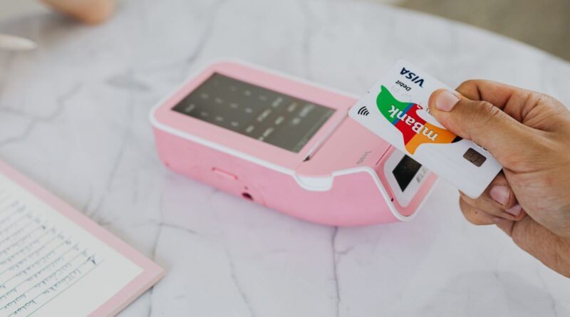 Hand tapping a Visa card on a pink contactless payment terminal