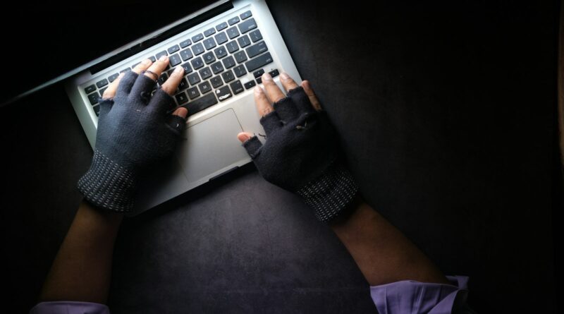 Hands in fingerless gloves typing on a laptop in the dark